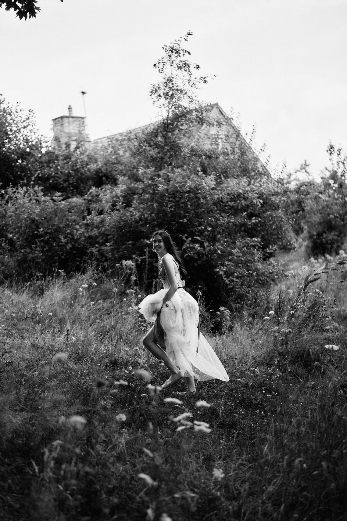A woman in a white wedding dress is running across a field.