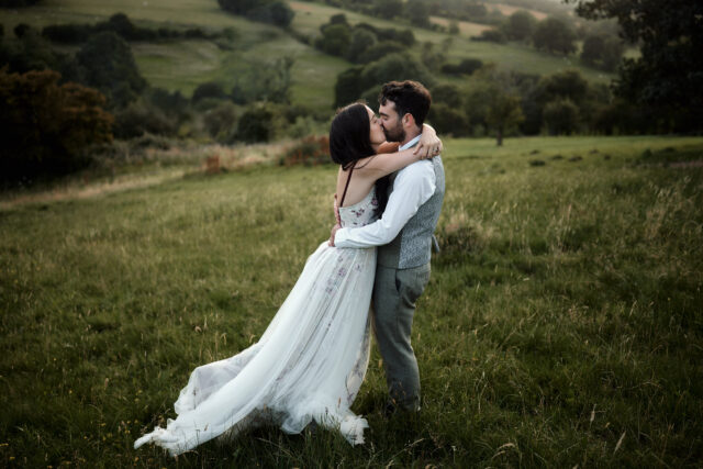 A couple getting married are sharing a kiss in an open field.