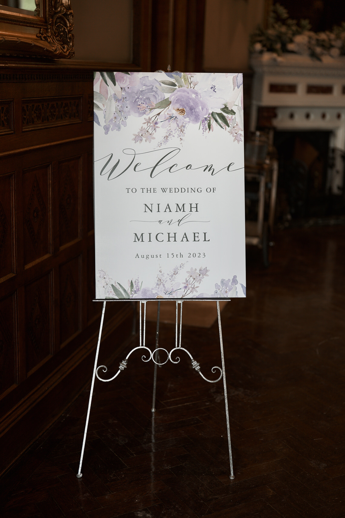 A welcome sign decorated with lavender flowers is placed on an easel.
