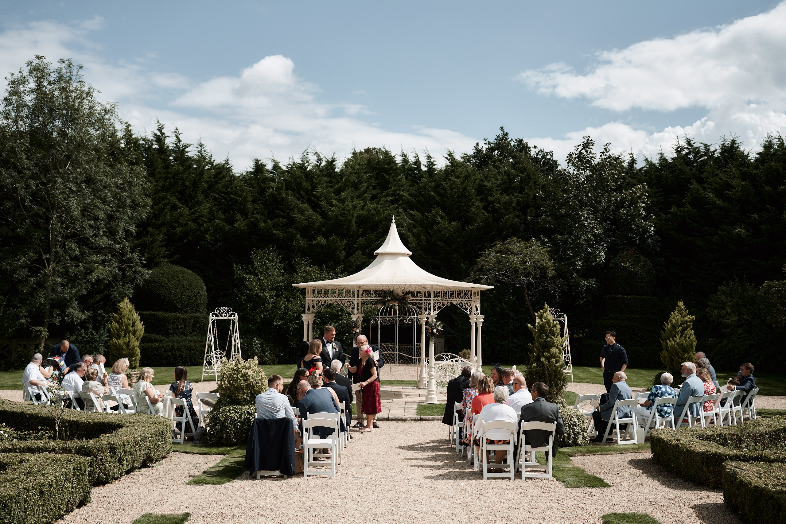 A wedding taking place in a garden that has a small roofed structure.