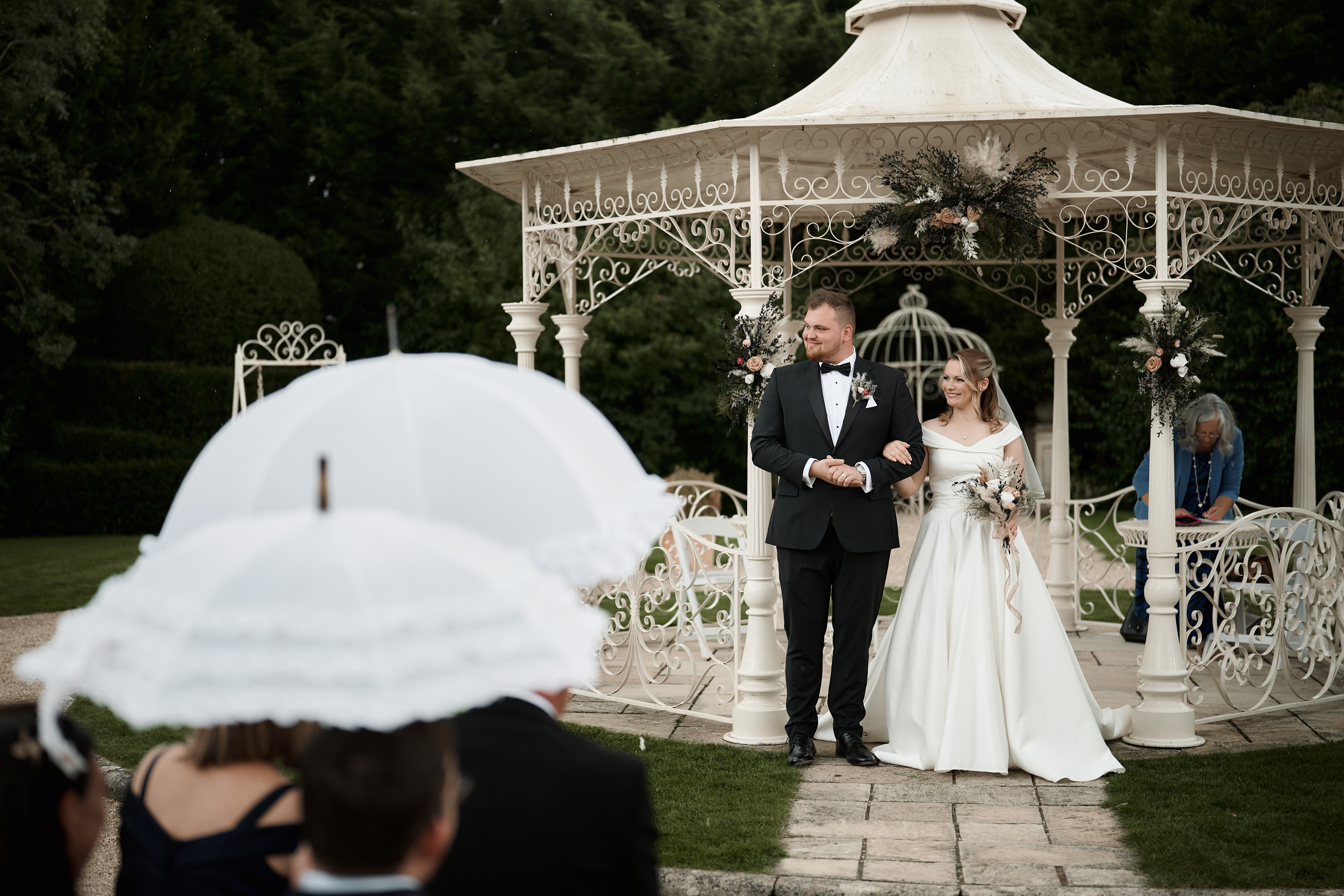 A couple getting married is standing under a pavilion with umbrellas.