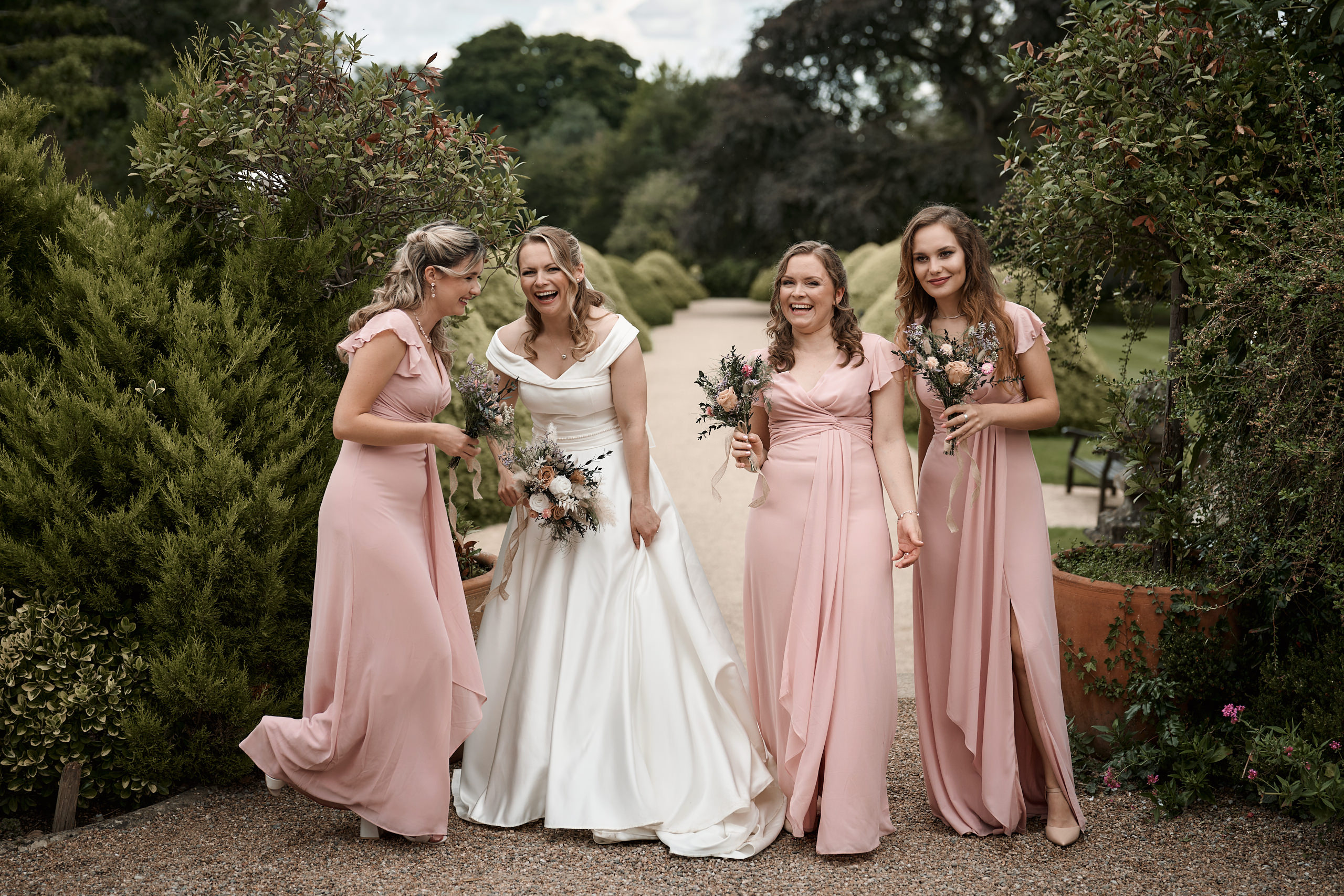 Four girls in pink bridesmaid dresses are in a garden.
