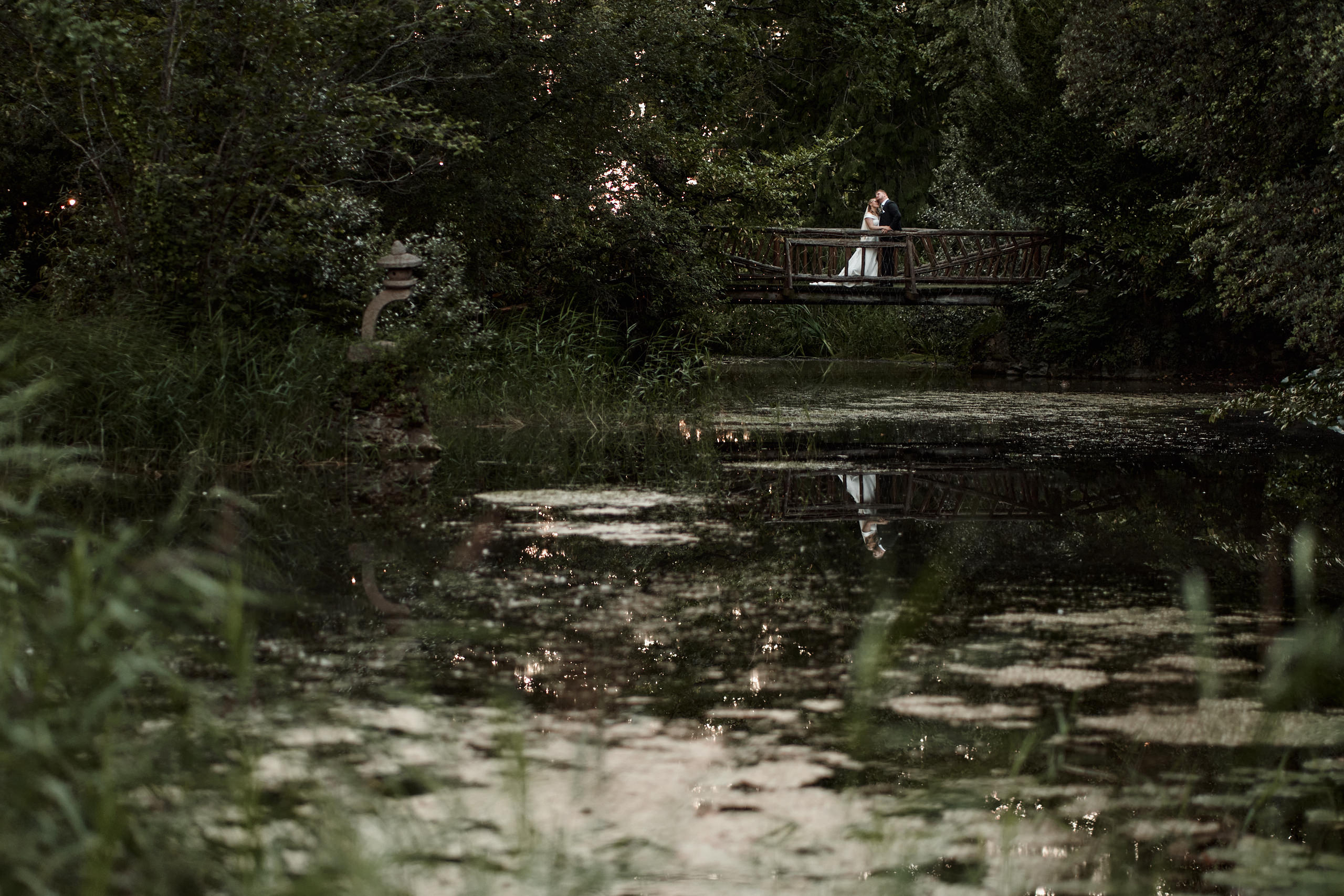 A couple getting married standing on a bridge above a pond.