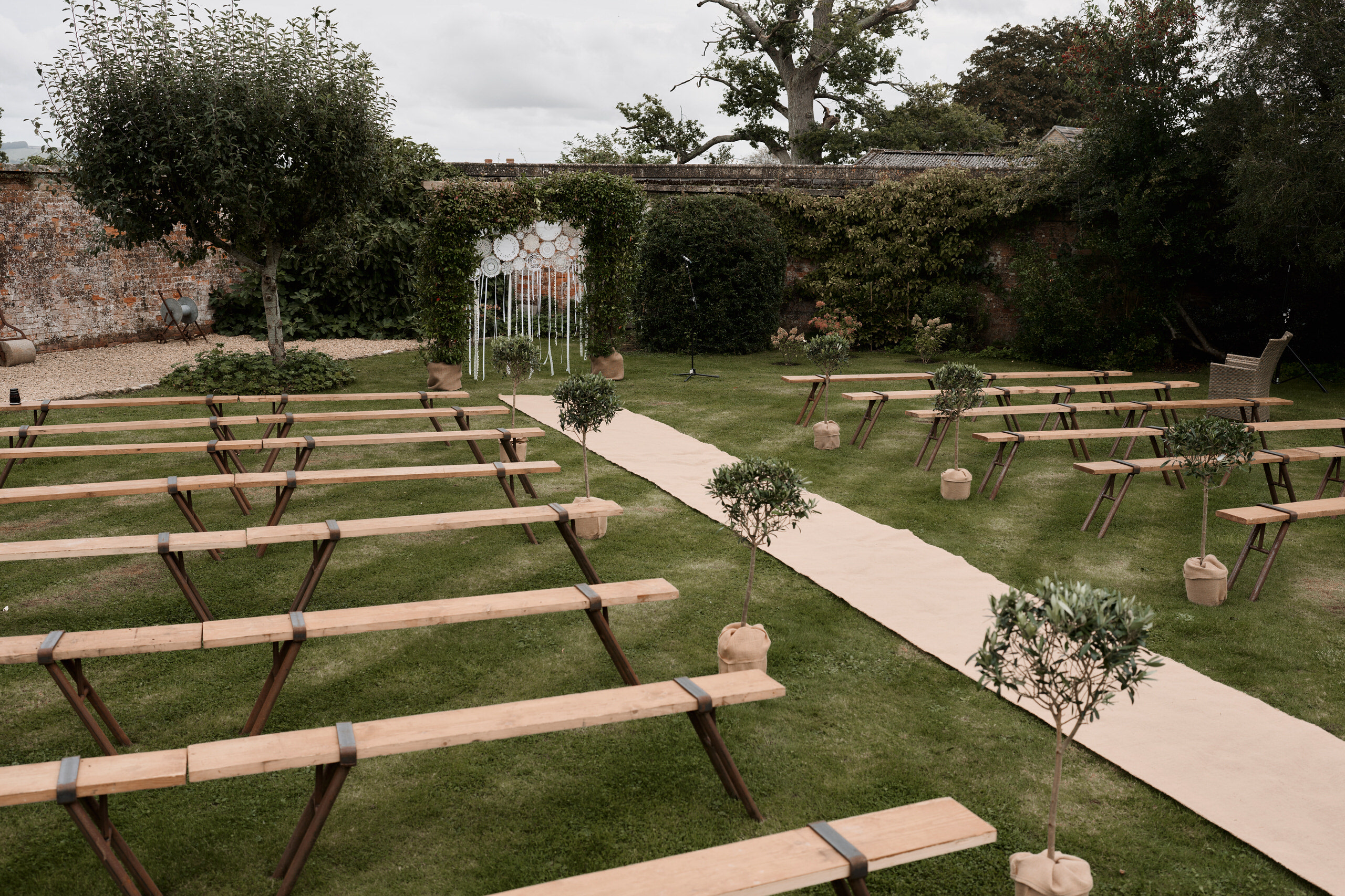 A wedding ceremony is being set up outside with wooden benches.