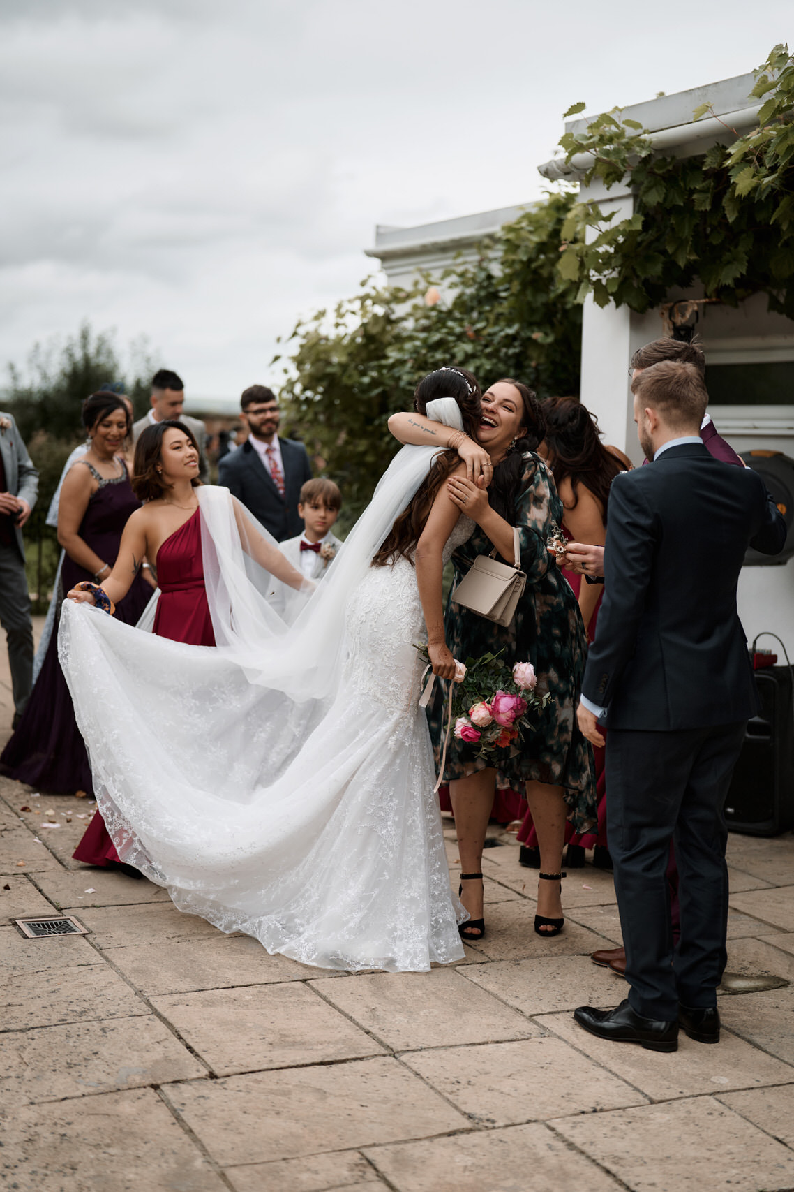 A bride and her bridesmaids are giving each other a hug in a courtyard.