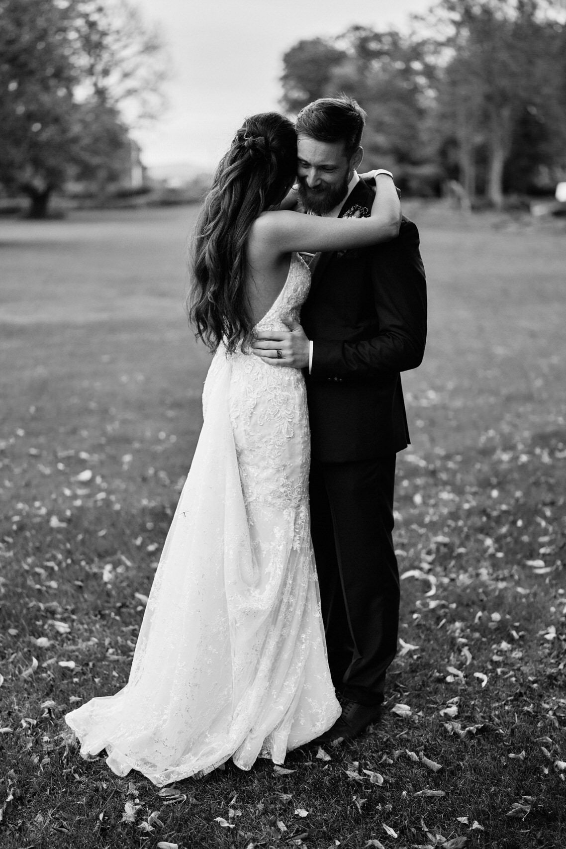 A black and white picture of a newly married couple embracing each other in a field.