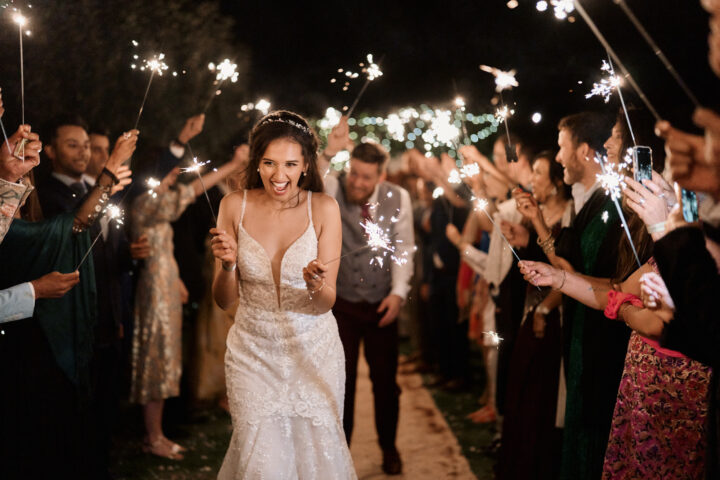 The bride and groom are happily running through a line of friends and family waving sparklers at their nighttime wedding party.