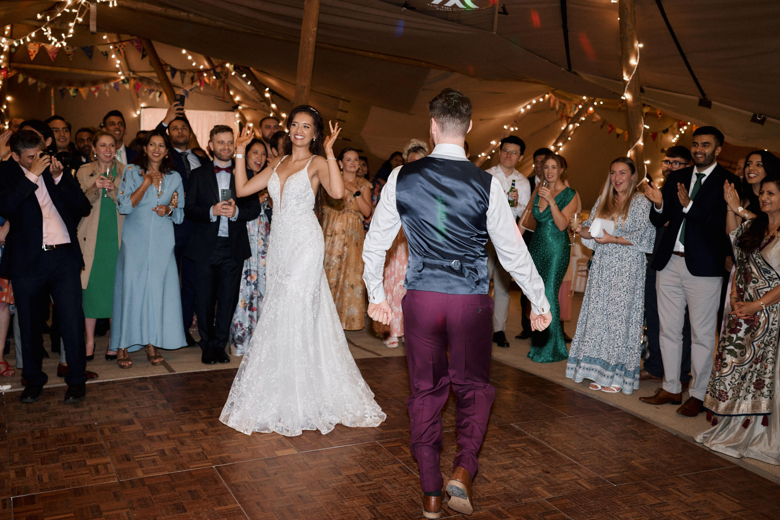 A couple is dancing on a wooden floor inside a tent at their wedding.