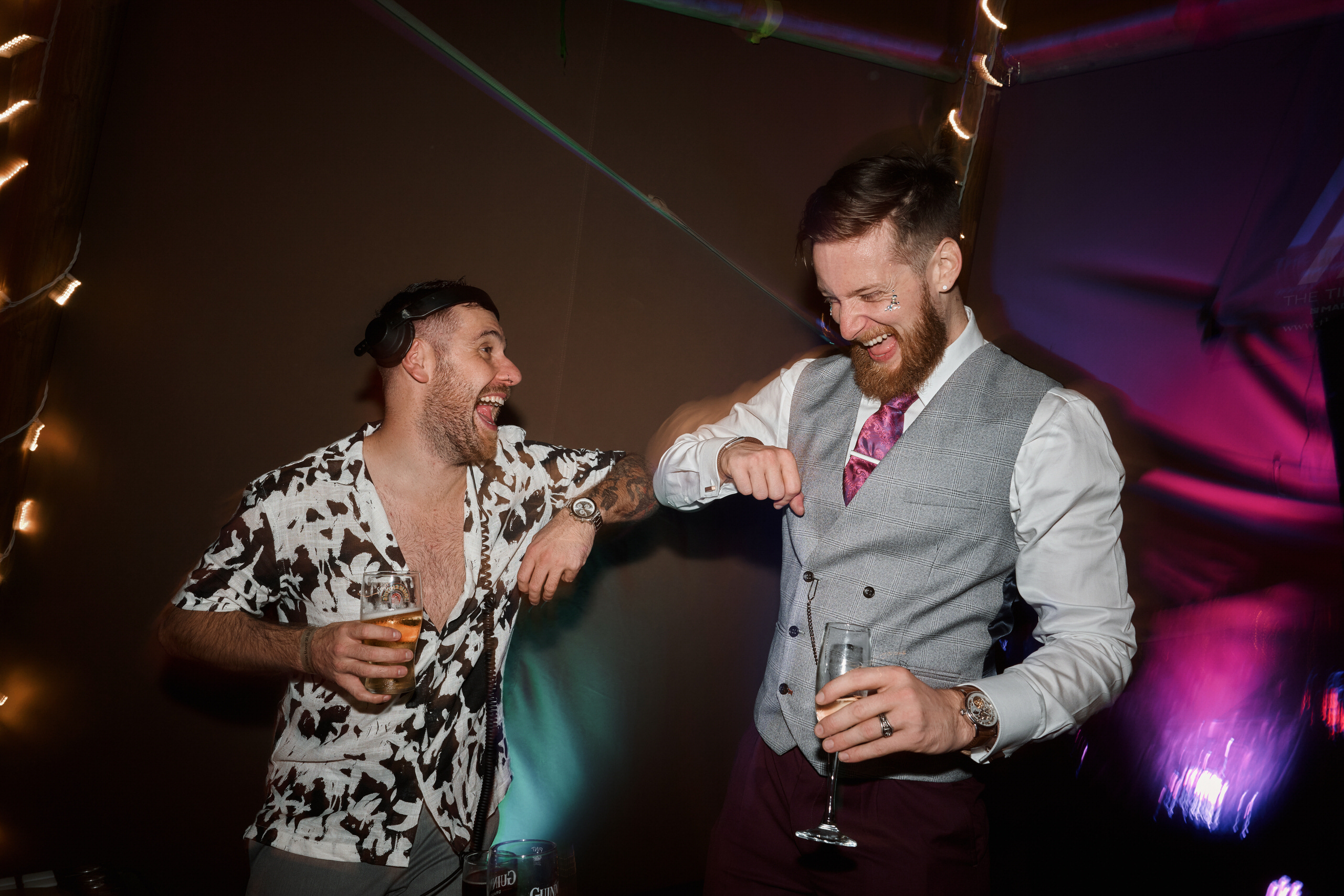 Two guys cracking up at a party inside a tent.
