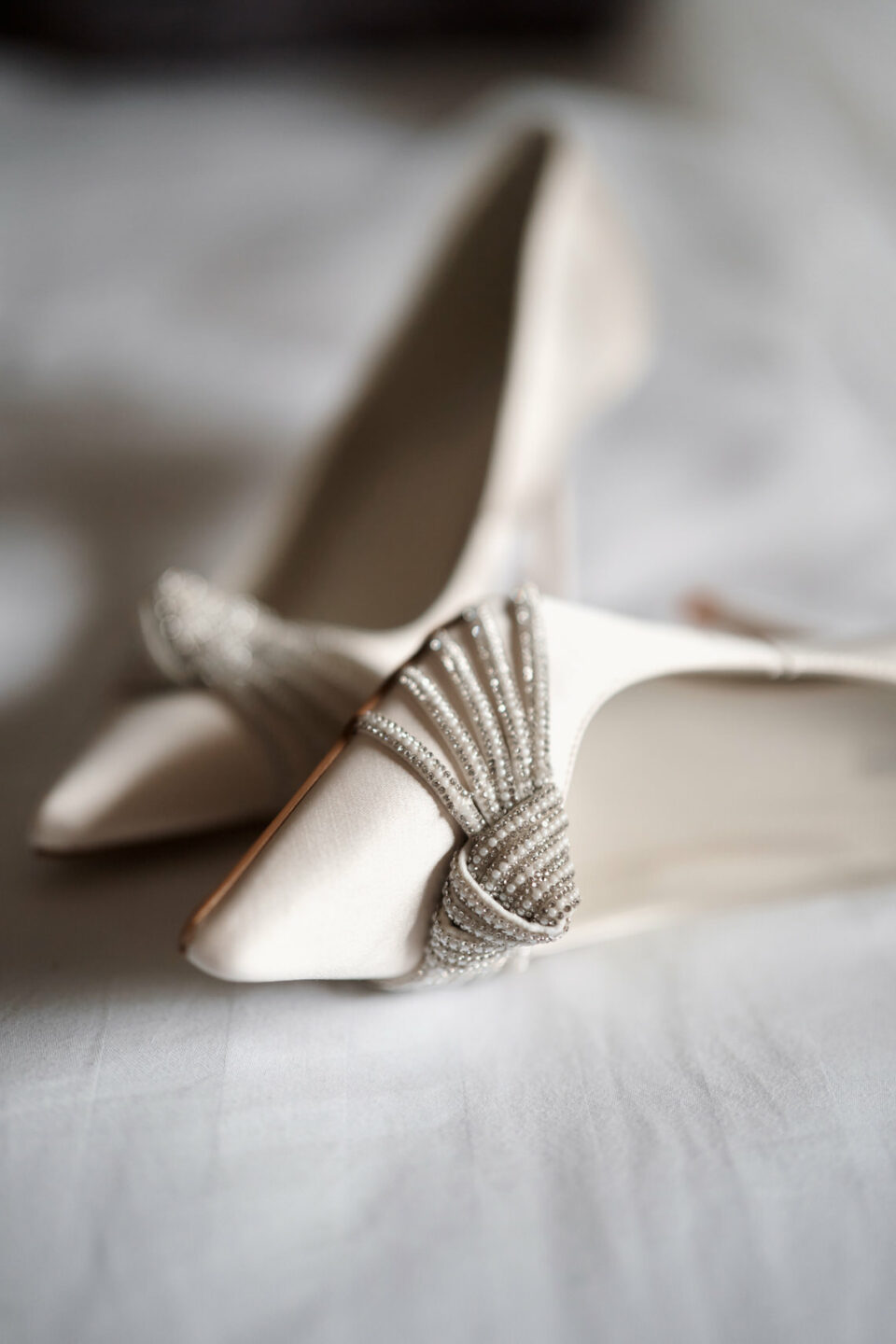 There's a pair of white wedding shoes on the bed.
