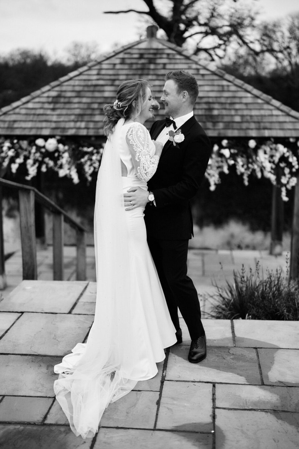 A couple getting married is smooching in front of a small outdoor structure.