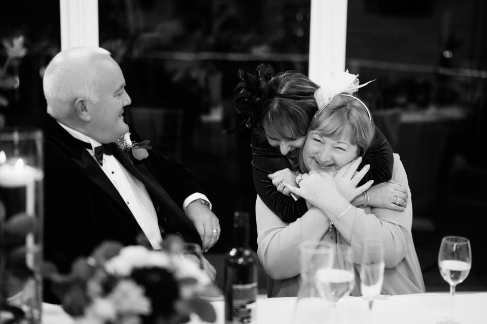 A lady is squeezing a guy in a loving way at a wedding.