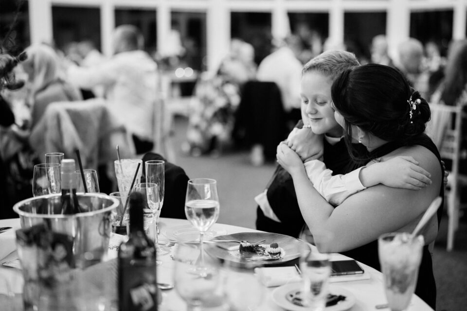A lady wrapping her arms around a kid at a wedding party.