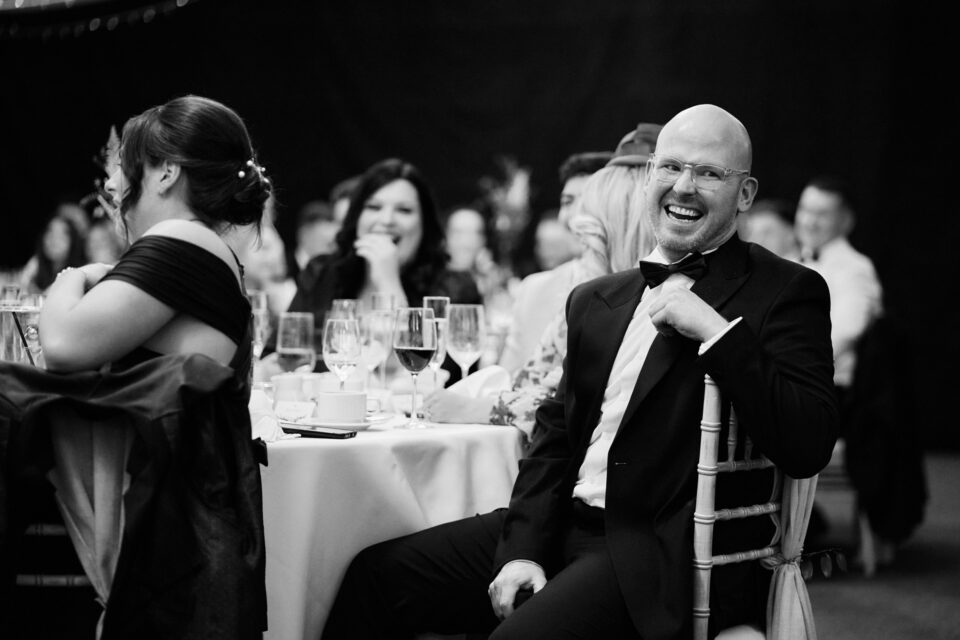 A black and white picture of a guy laughing at a table.