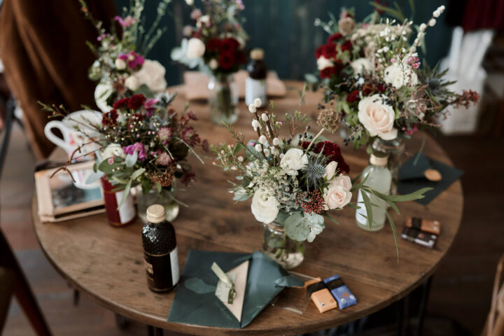 A laid-back table setting with mismatched flower displays in different vases, random paper stuff, and other small personal knick-knacks meant to make the meal more enjoyable.