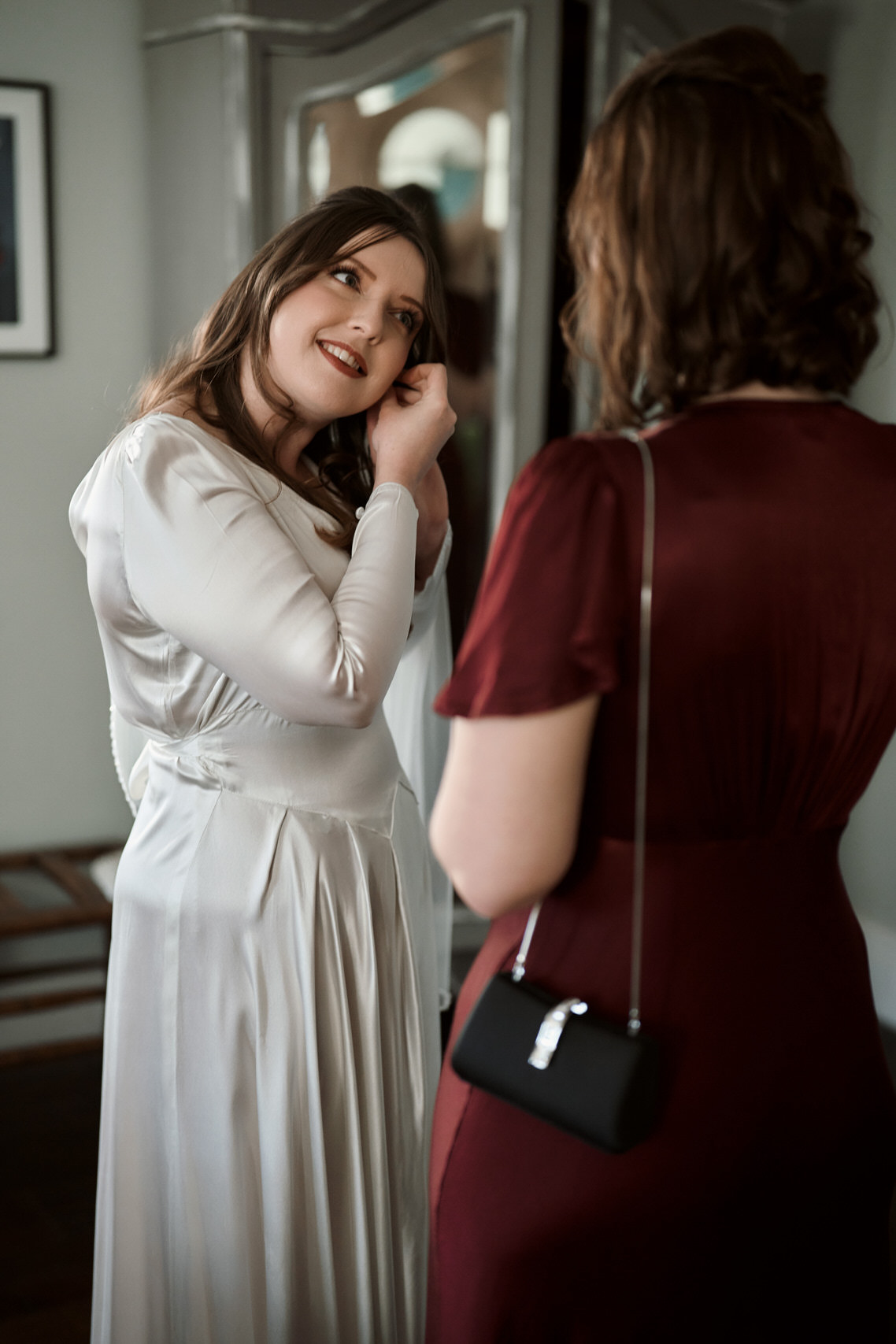 A lady in a white dress is looking at another lady in the mirror.