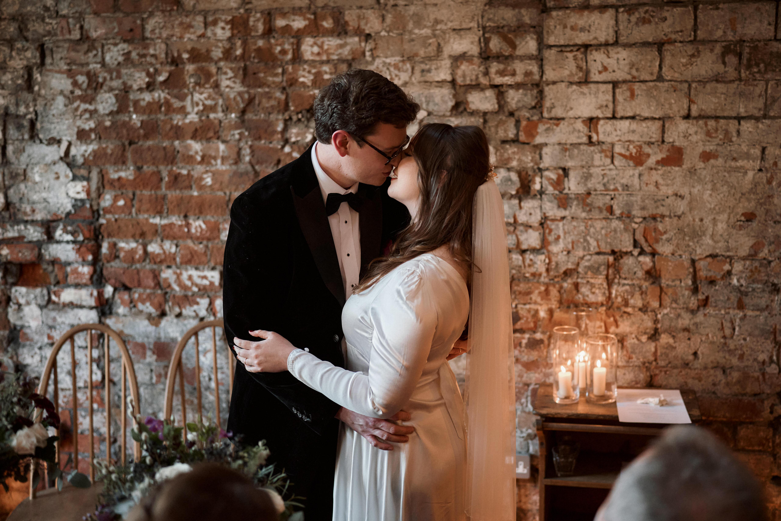 A couple is smooching in front of a brick wall on their wedding day.