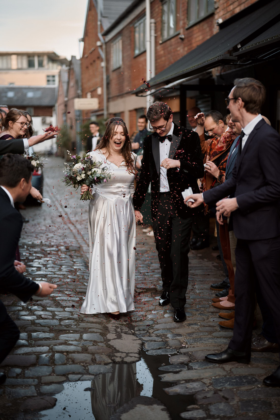 A couple just married is strolling down a street with stone pavement.