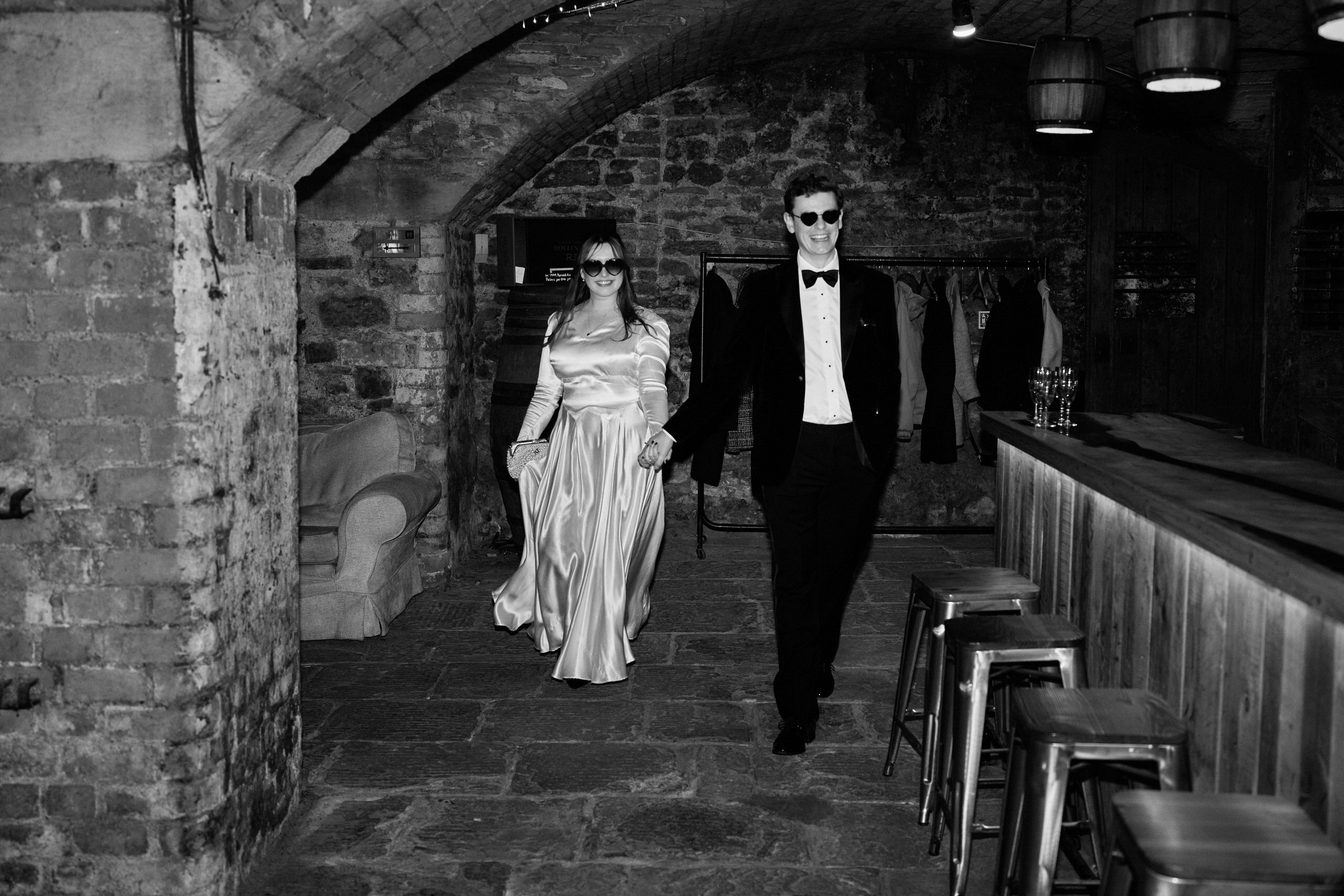A black and white picture of a newlywed couple walking down a hall.
