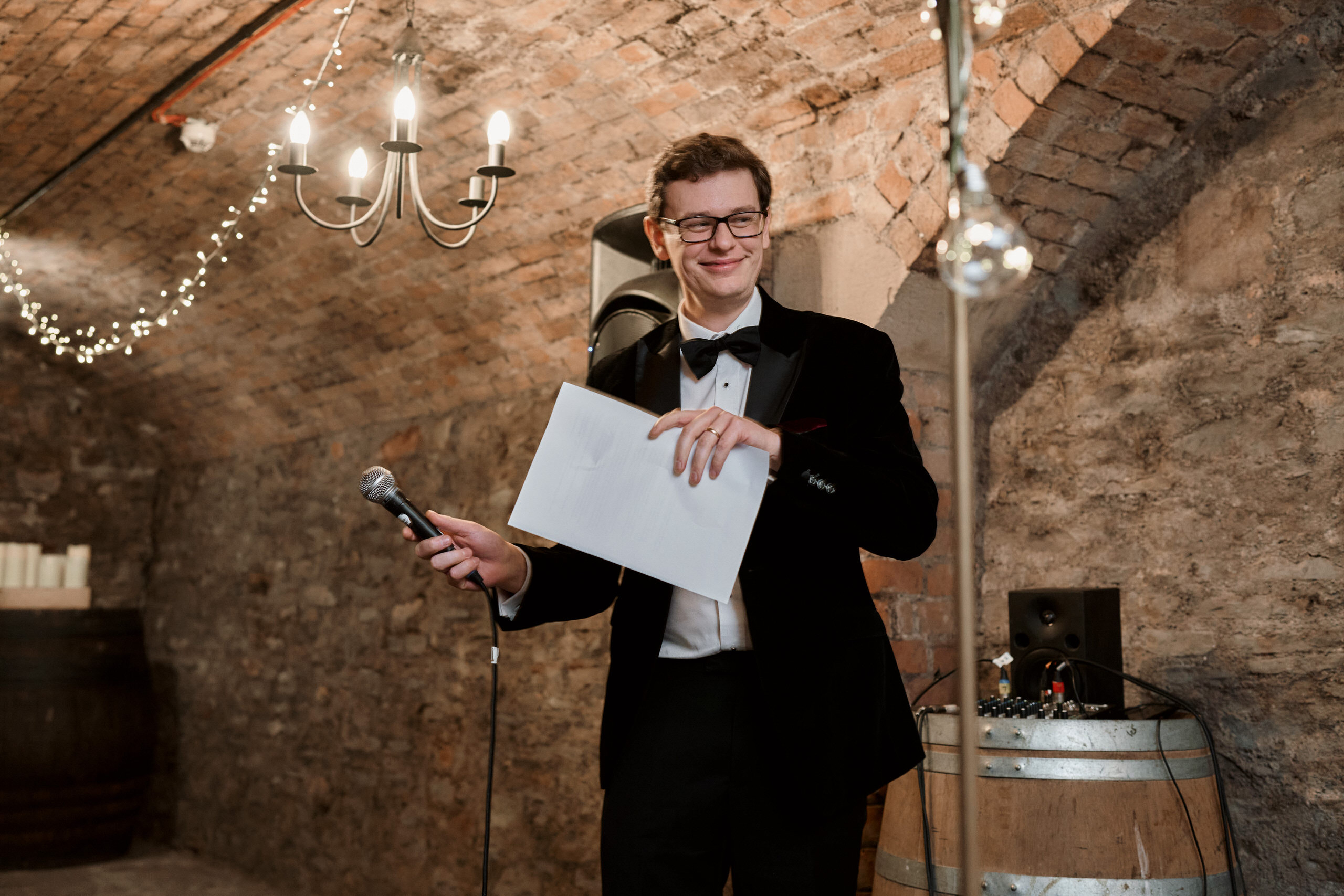 A guy in a suit is holding a mic in a room where they store wine.