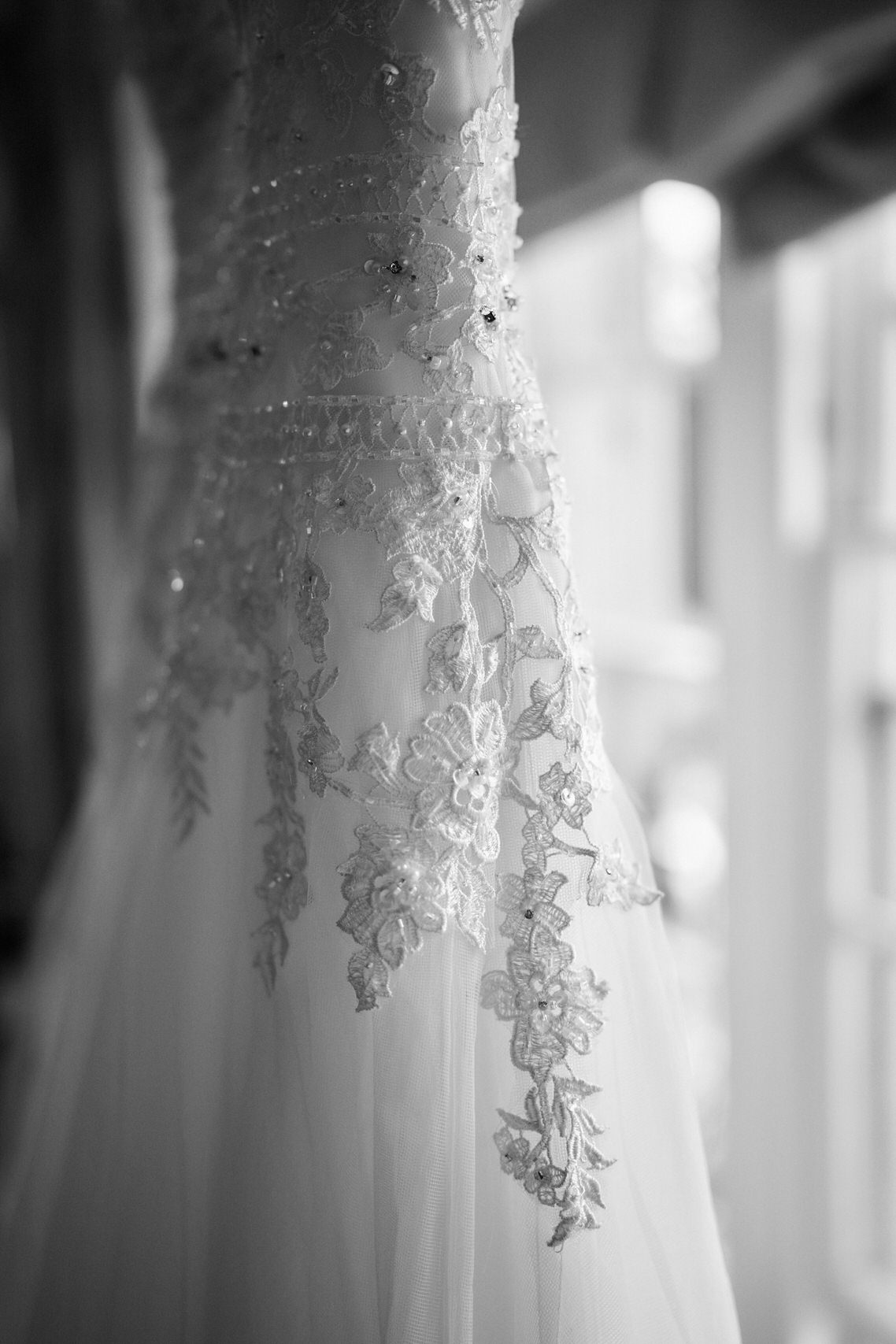 A wedding dress is hanging in a window, shown in a black and white picture.