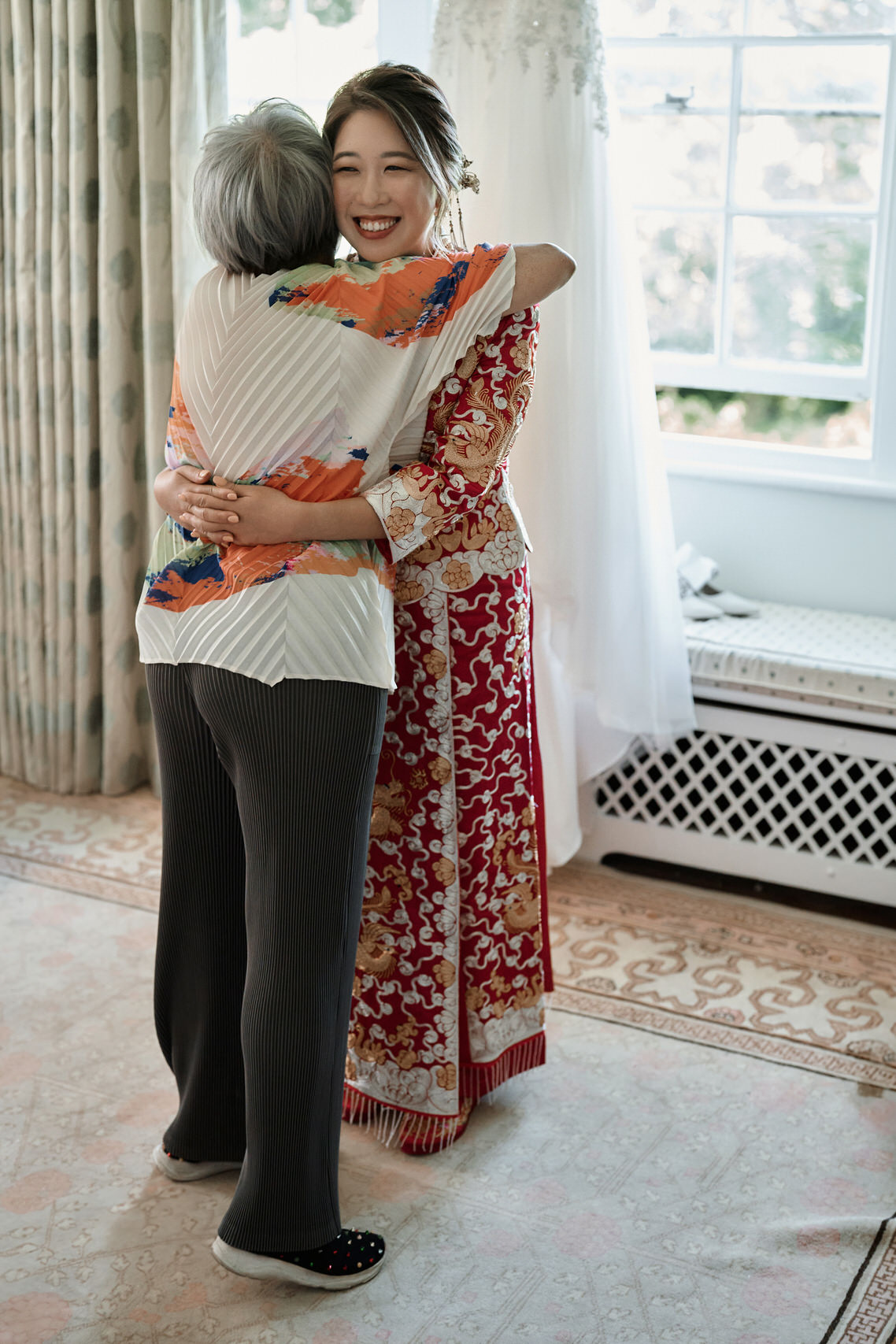 A bride and her mom are hugging in a room.