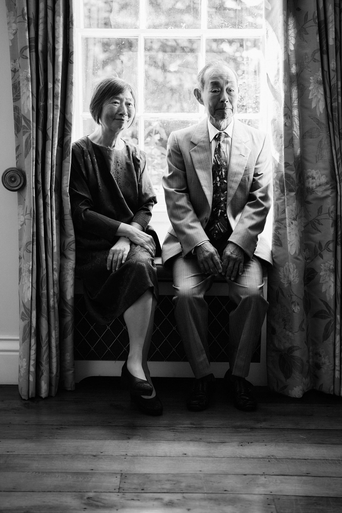 A picture in black and white of a couple sitting by a window.