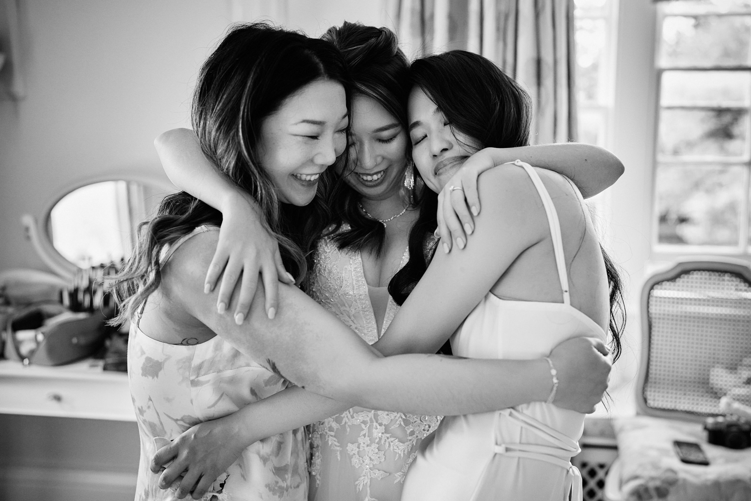 A black and white picture of three bridesmaids gives each other a hug.