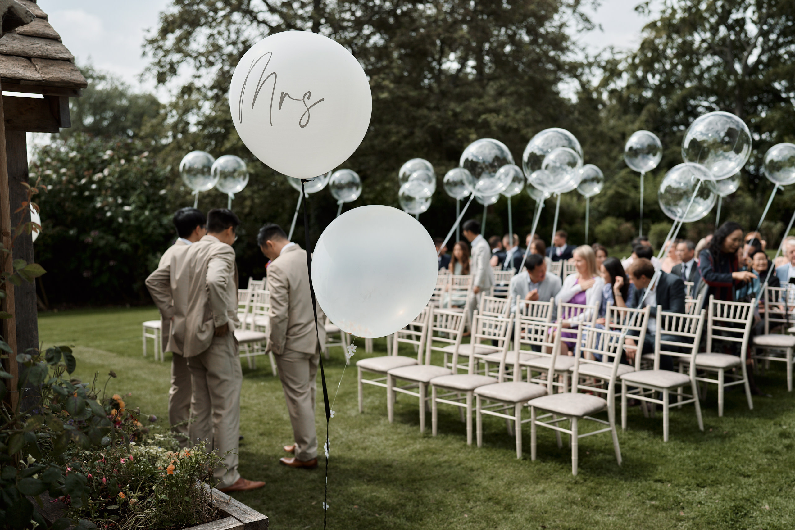 A wedding happening outside with balloons on the grass.