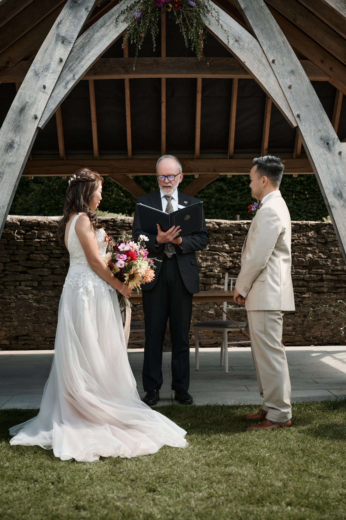 A man and a woman getting married make promises to each other near a wooden outdoor structure.