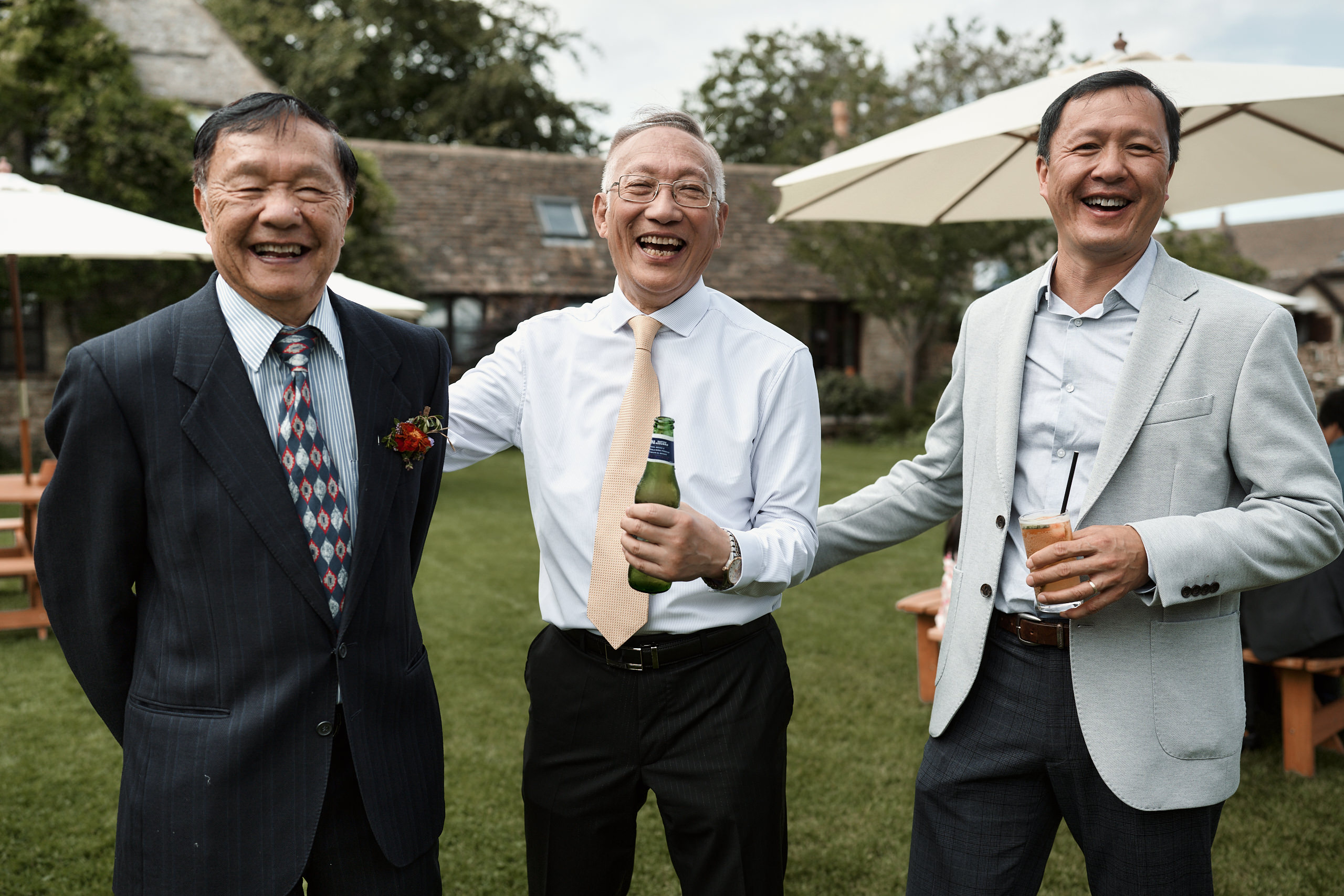 Three Asian guys in suits cracking up at a wedding.