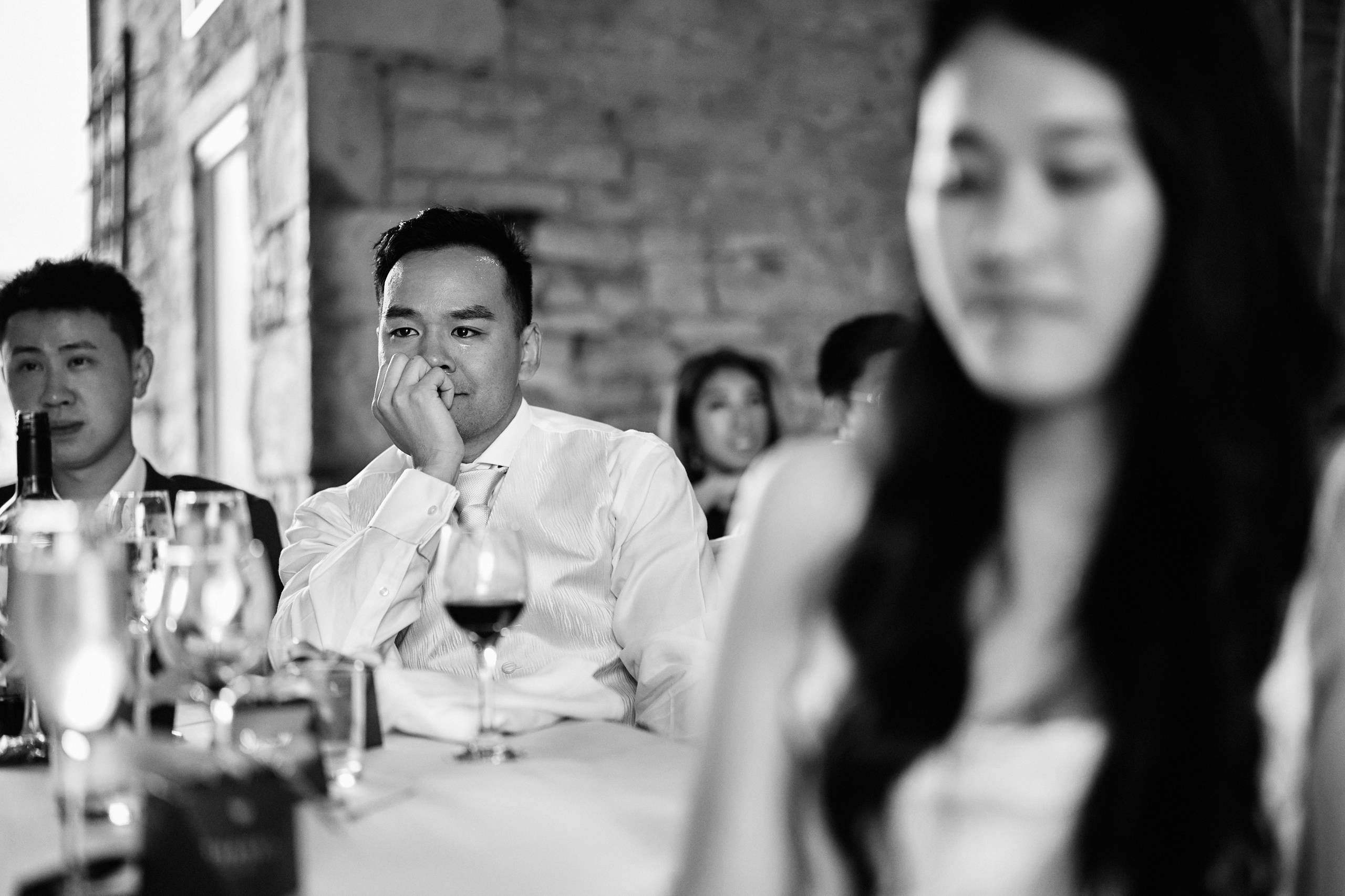 A guy is tearing up sitting at a table during a wedding.