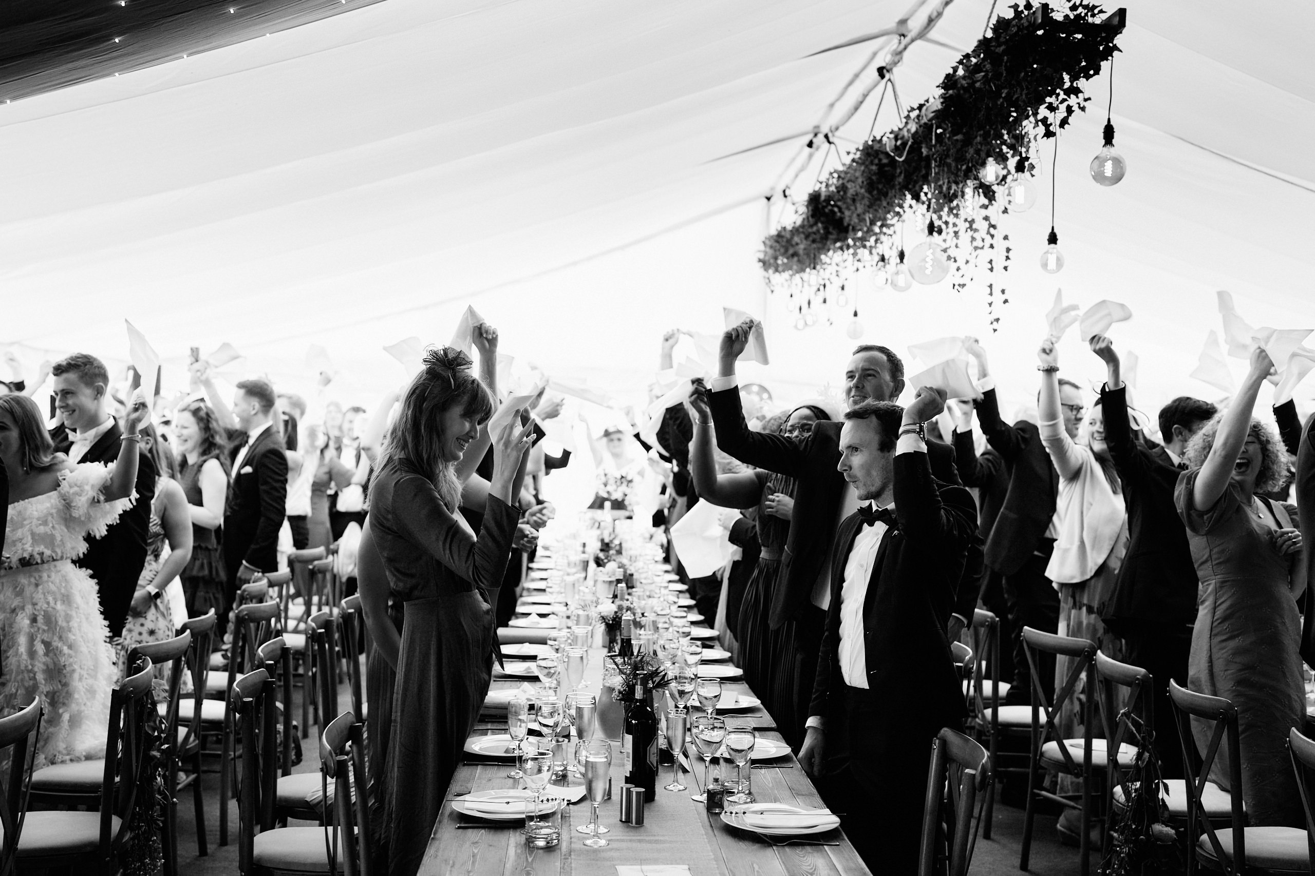 A black and white picture of folks raising their hands at a wedding.