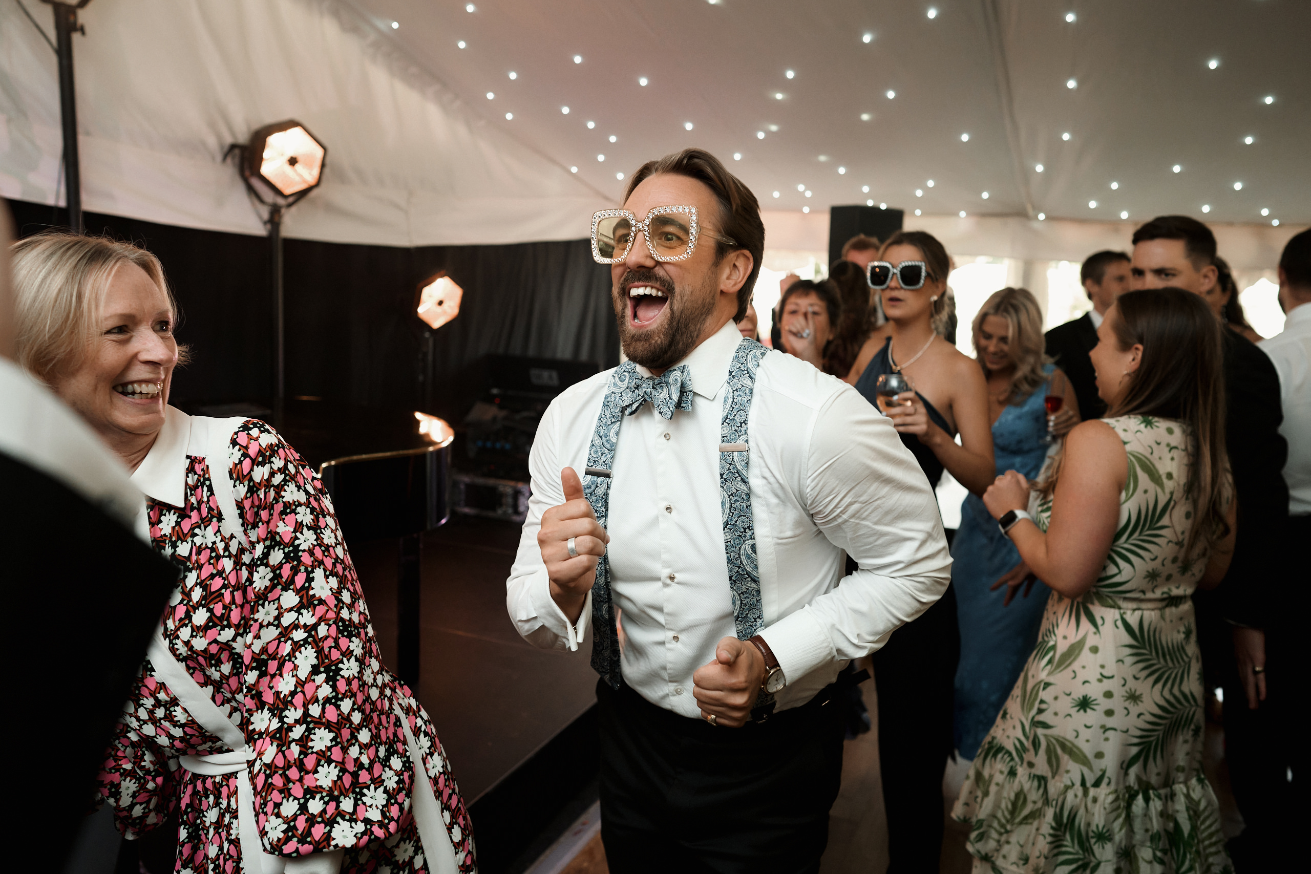 A guy in sunglasses and a tie is busting some moves in a tent.