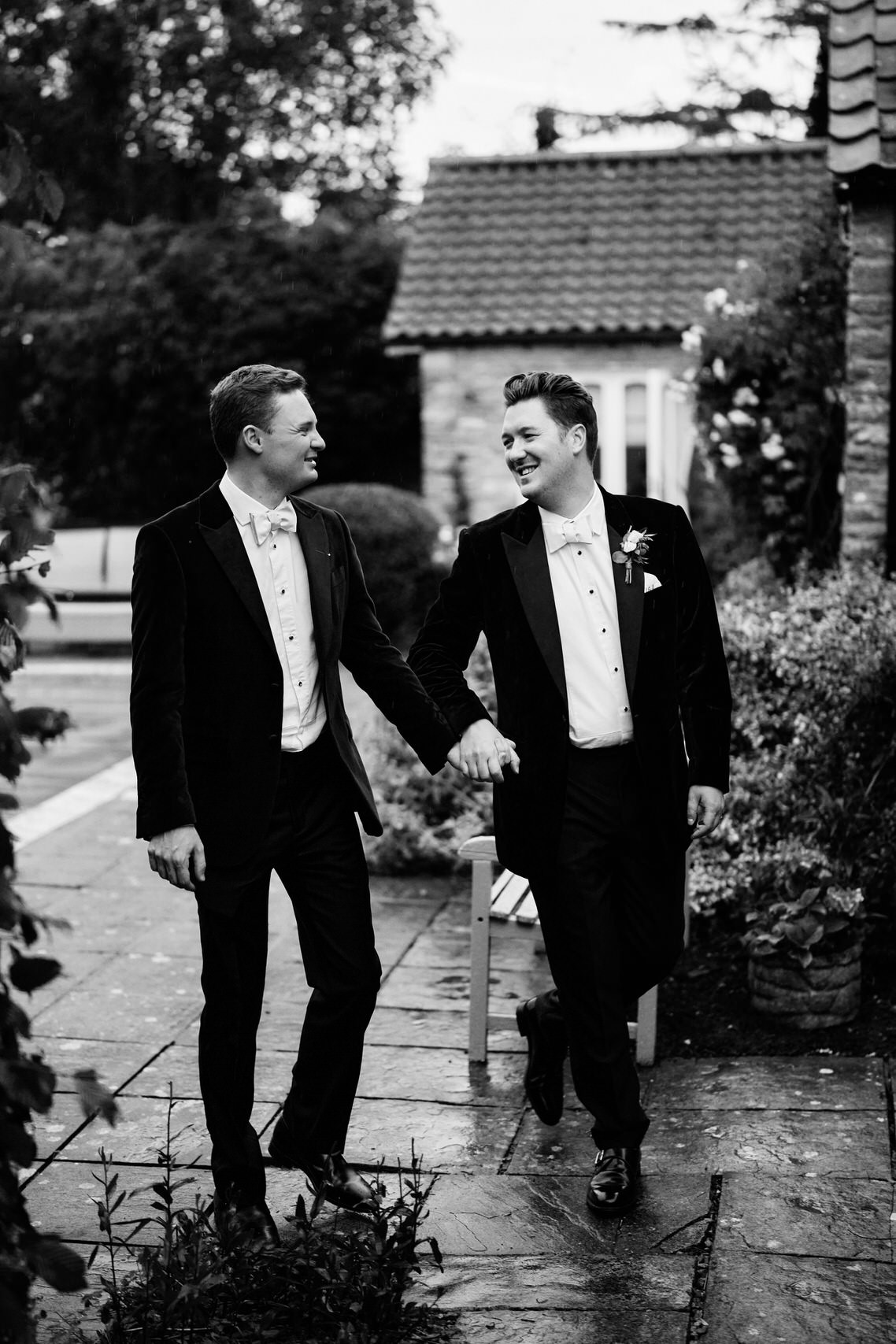 Two guys in suits holding hands outside a home.