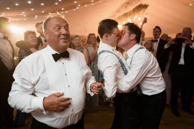 Two guys are embracing each other on the dance floor at a wedding.