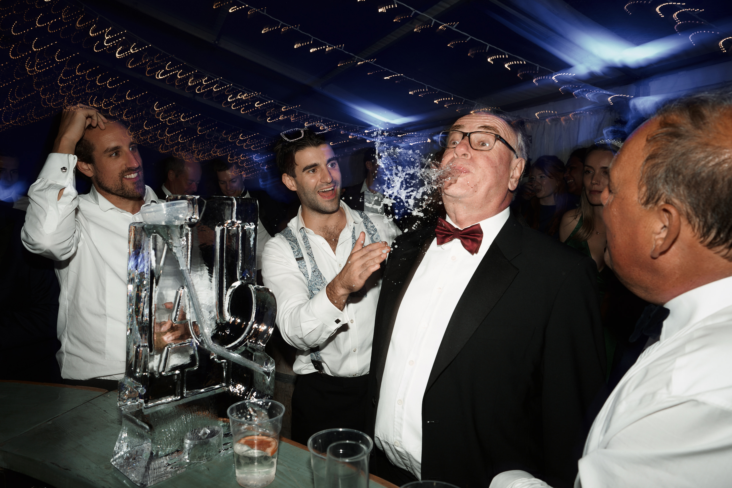 A guy in a fancy suit is blowing bubbles at a party.