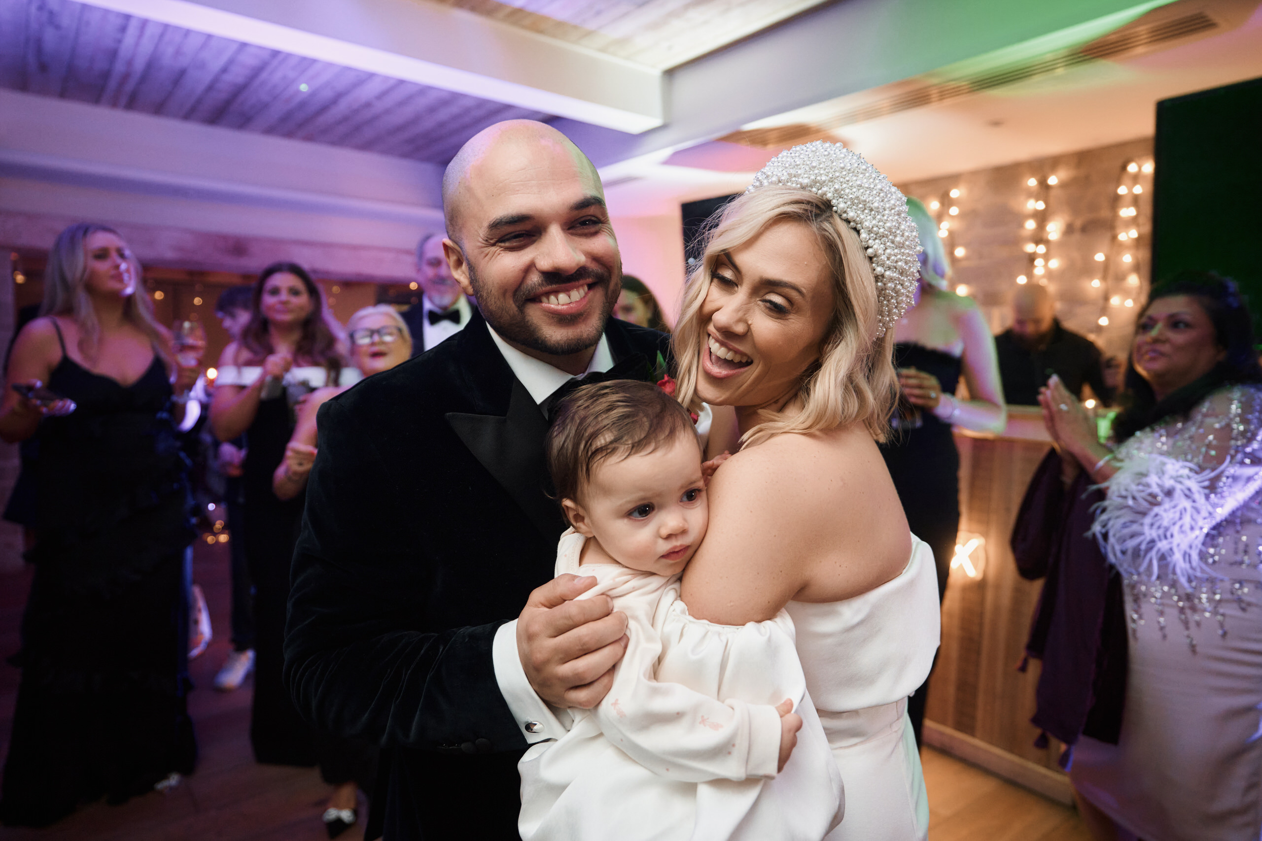 A couple holding a baby on the dance floor at their wedding.