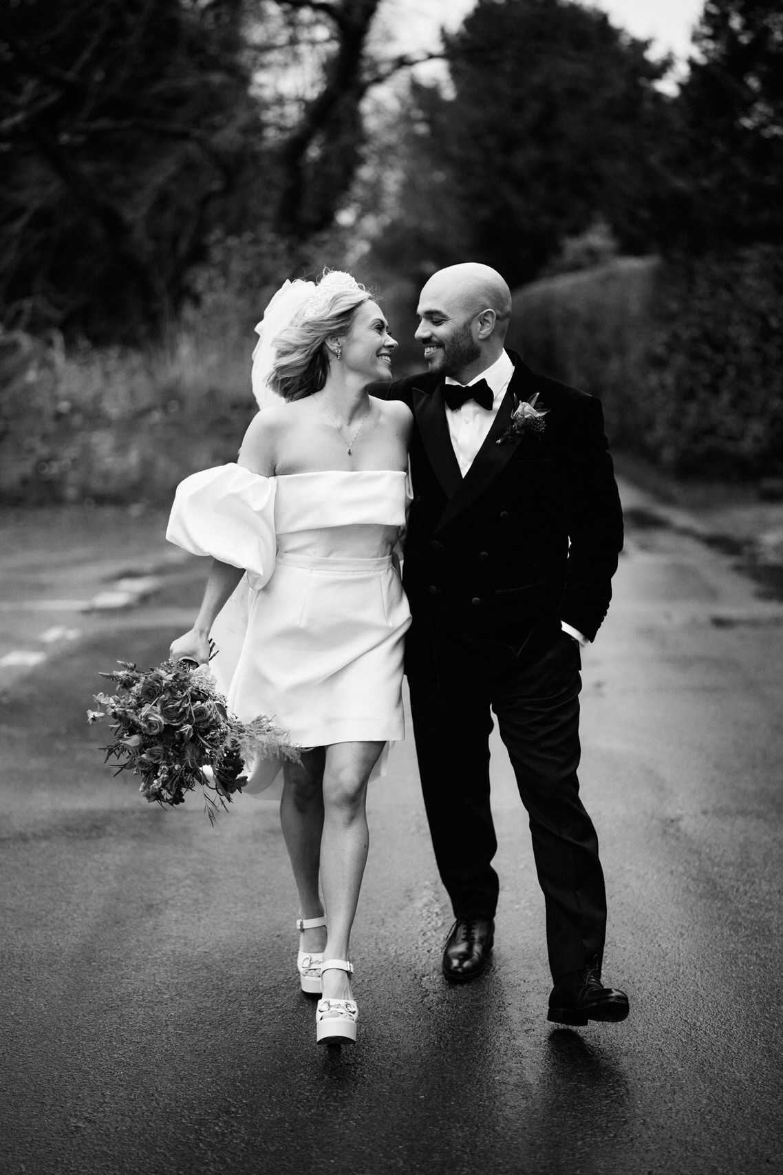 A black and white picture of a newlywed couple walking in the rain.
