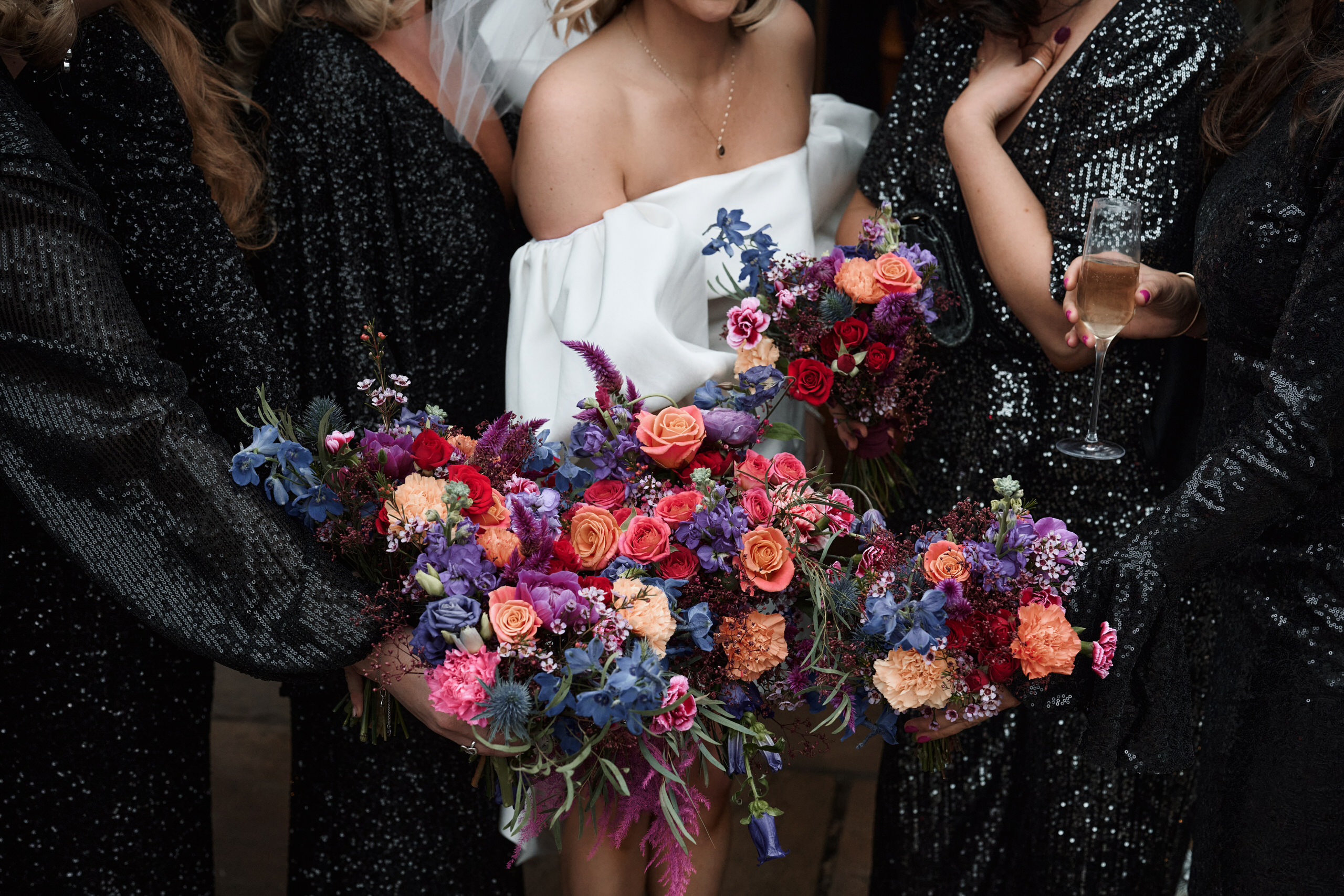 A bunch of bridesmaids holding flowers and wearing black sparkly dresses.