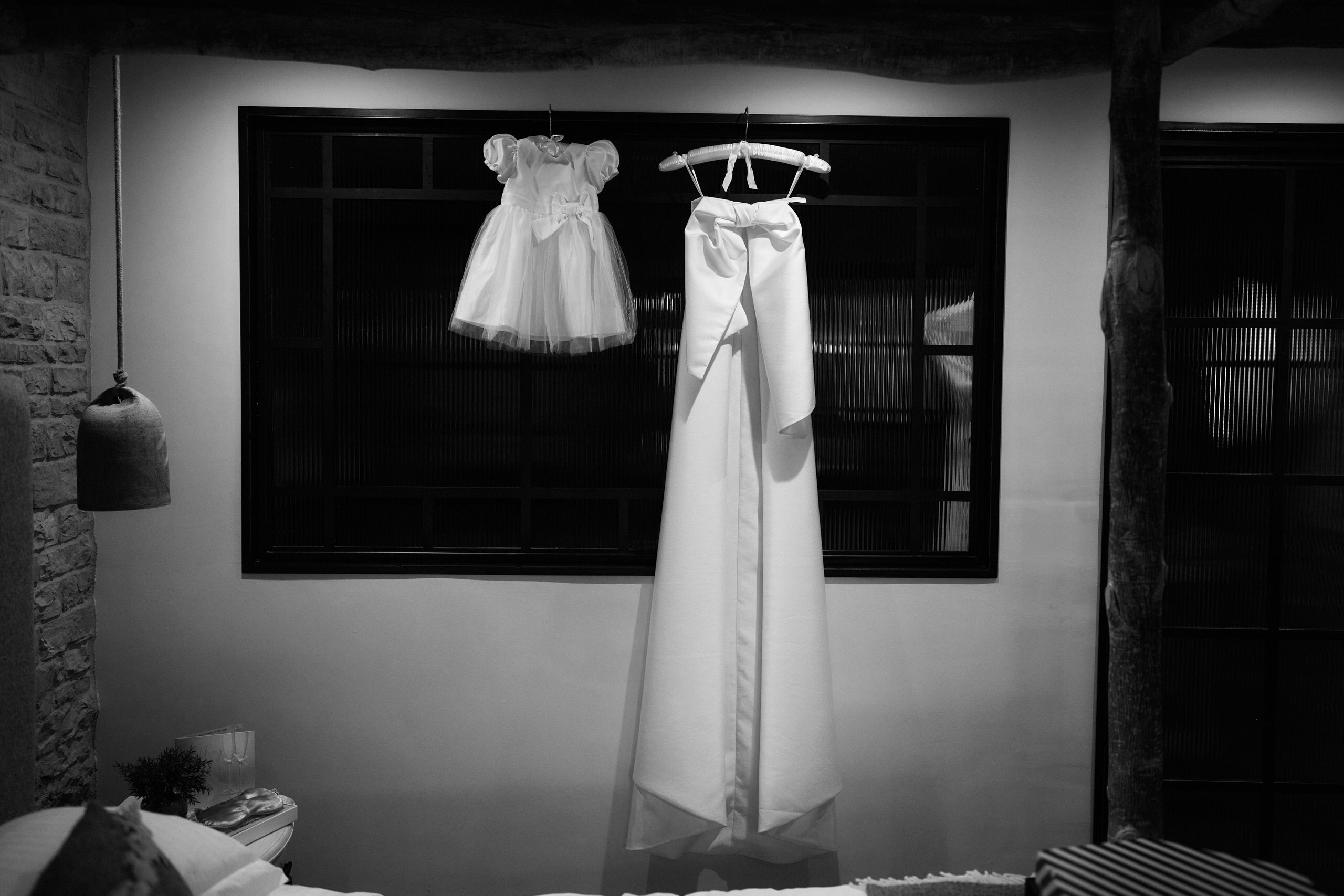A wedding dress is hanging in a window in a black and white picture.